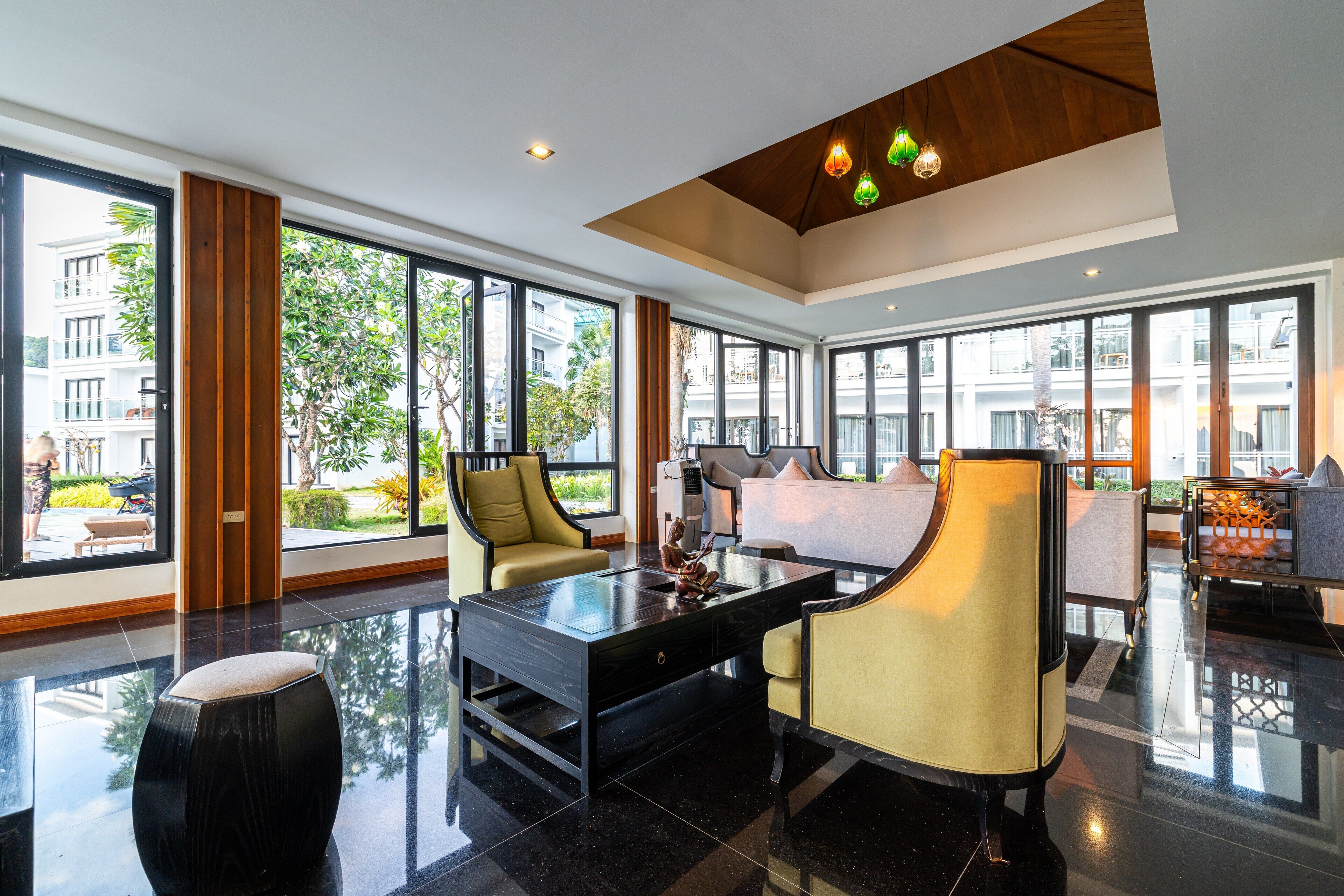 Un moderno vestíbulo de hotel con una mesa de centro de vidrio, dos sillones, un sofá y grandes ventanales con vistas a la ciudad.