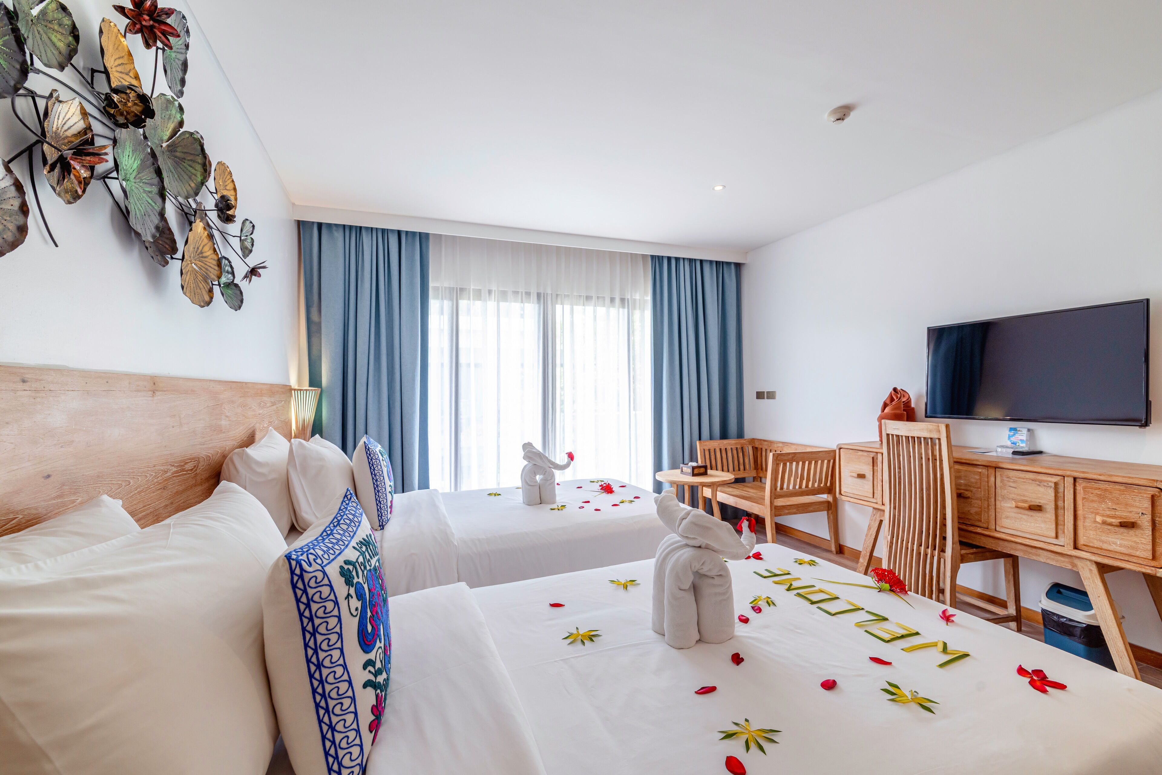 Ein Hotelzimmer mit zwei Betten, einem Schreibtisch, einem Sessel, einem Fernseher und einem großen Fenster mit Vorhängen.
