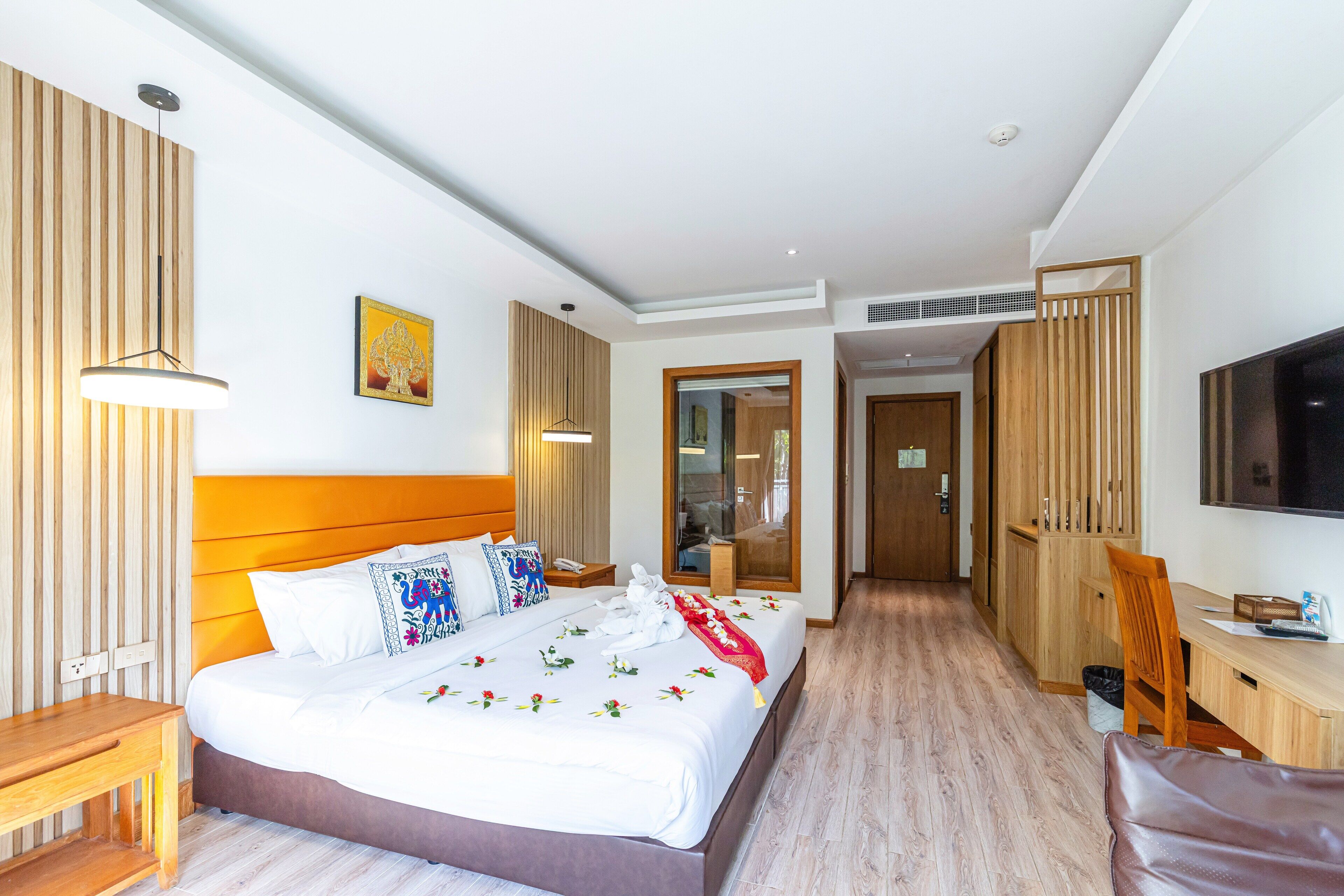A hotel room with a large bed, wooden headboard, bedside table, and a desk with a chair.