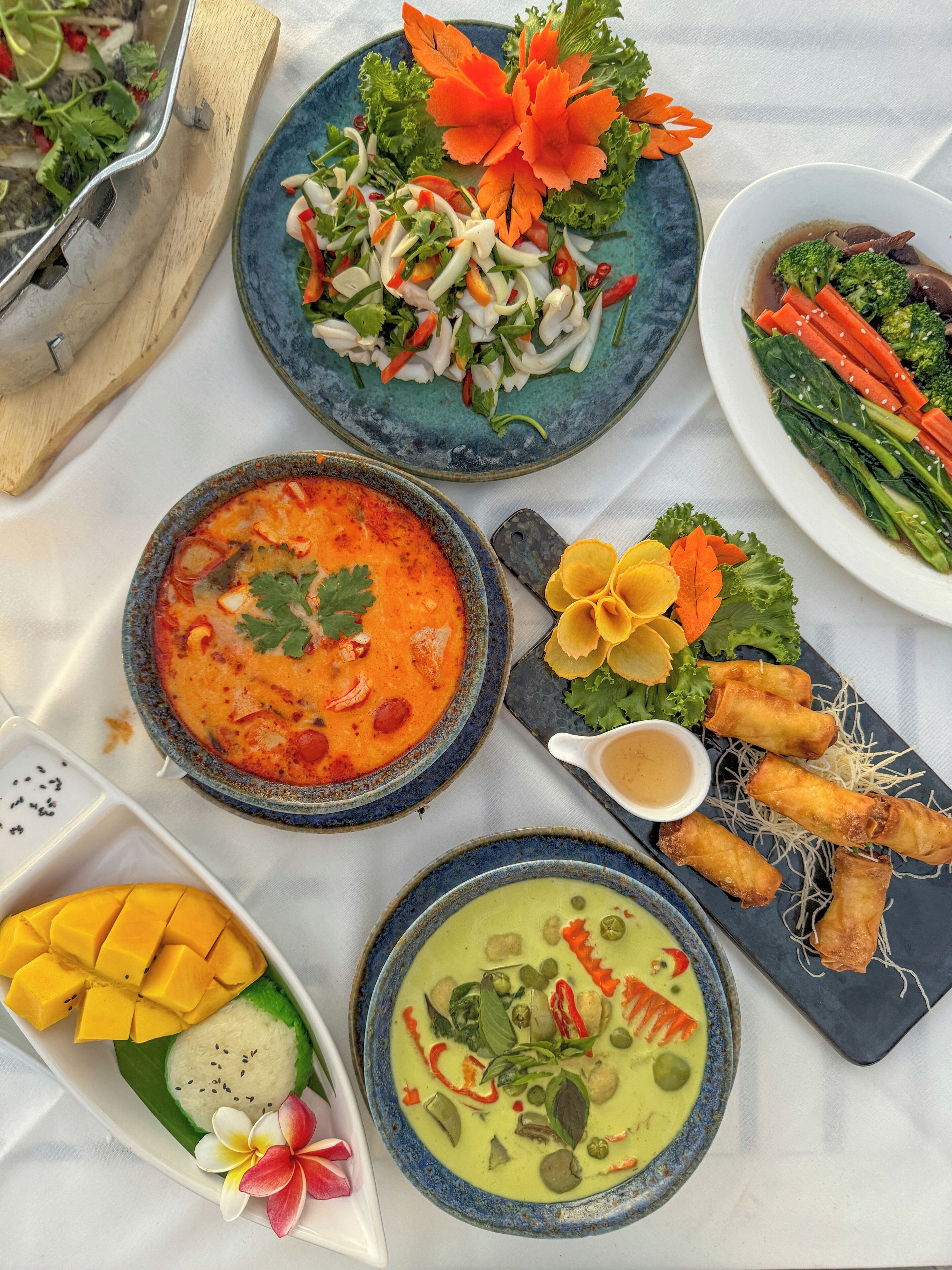 A table with various dishes including a bowl of soup, a plate of salad, and a plate of spring rolls.