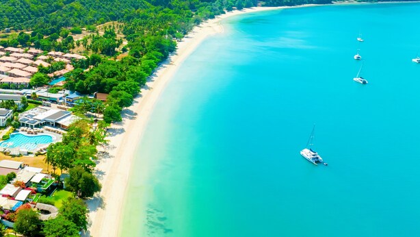 An aerial view of a coastal resort with a sandy beach, a swimming pool, and several boats anchored in the water. - Royal Yao Yai Island Beach Resort -sha Extra Plus+ (Ko Yao)