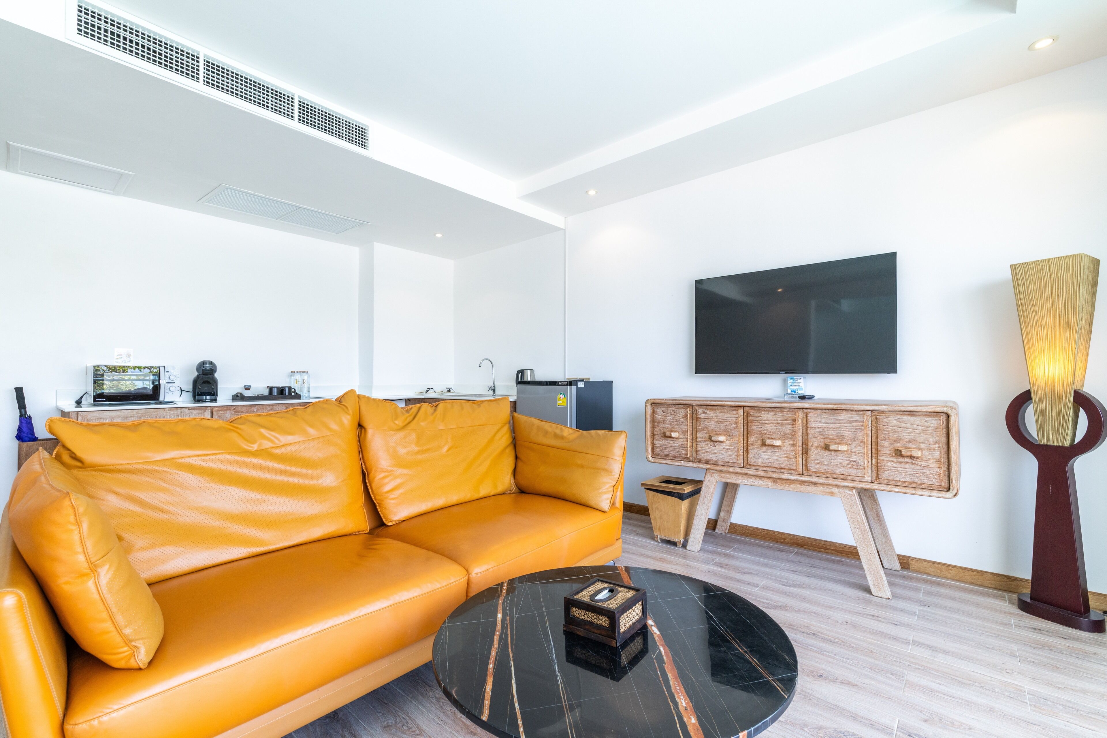A modern living room with a leather sofa, a round coffee table, a flat-screen TV, and a wooden cabinet.