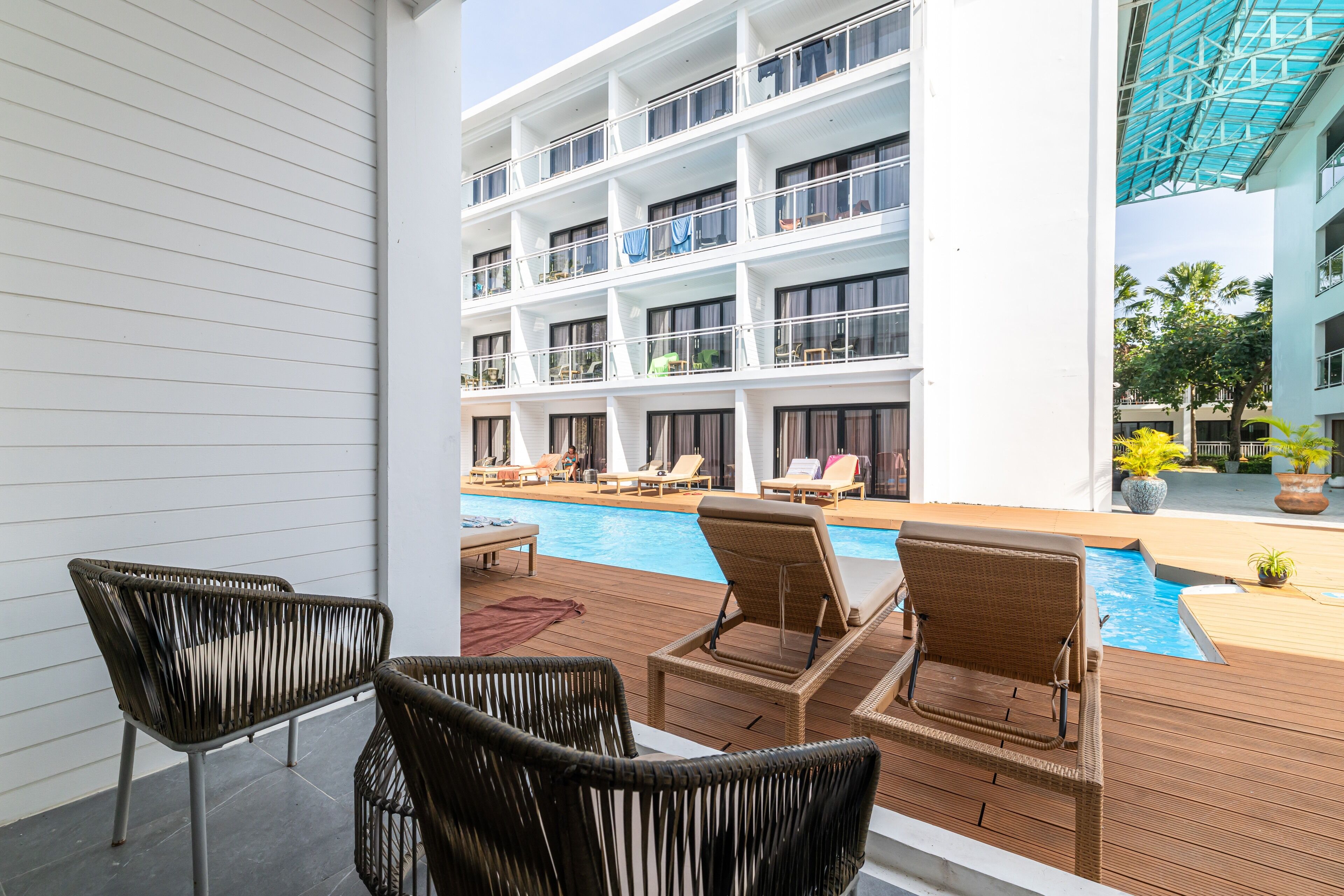 A poolside area with wicker chairs, a pool, and a multi-story building with balconies in the background.