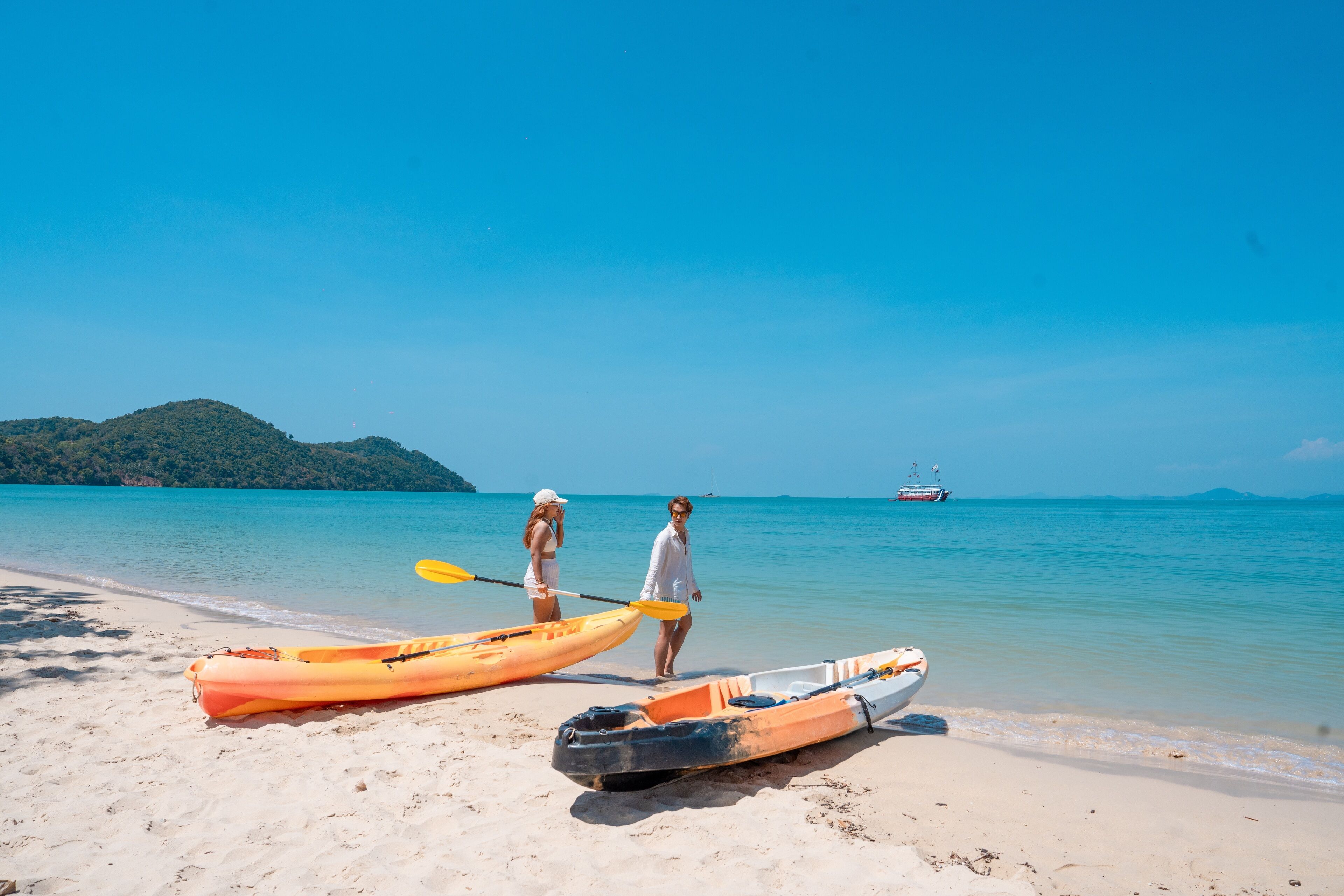 A beach with kayaks and a boat, a clear sky, and a distant ship.