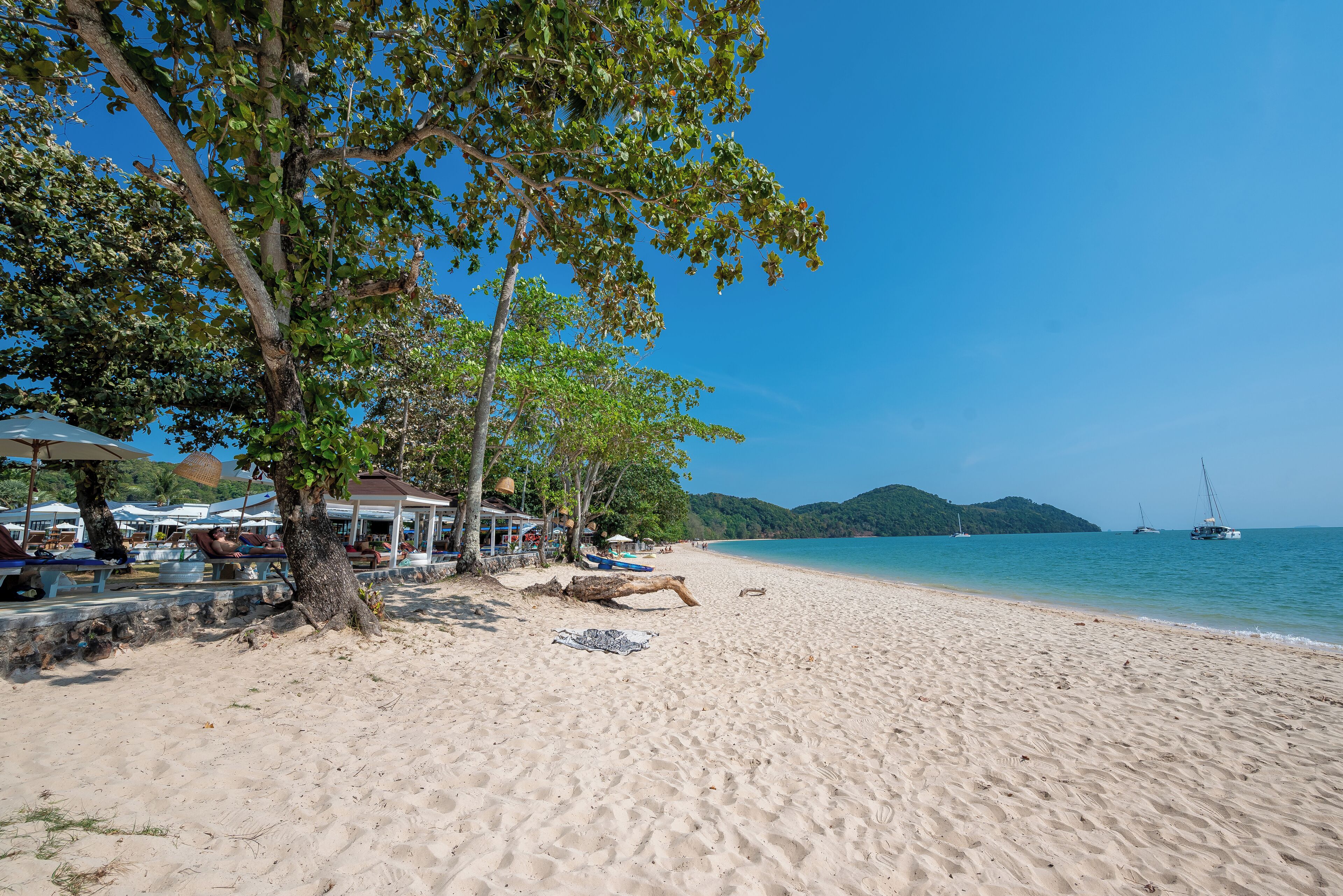 Une plage avec un rivage sablonneux, des parasols et quelques bateaux sur l’eau.