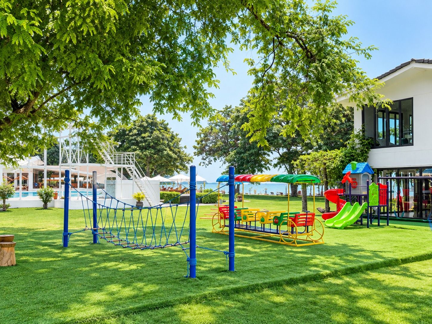 Ein Spielplatz mit einer Seilnetzkonstruktion, Rutschen und einem Gebäude mit großen Fenstern.