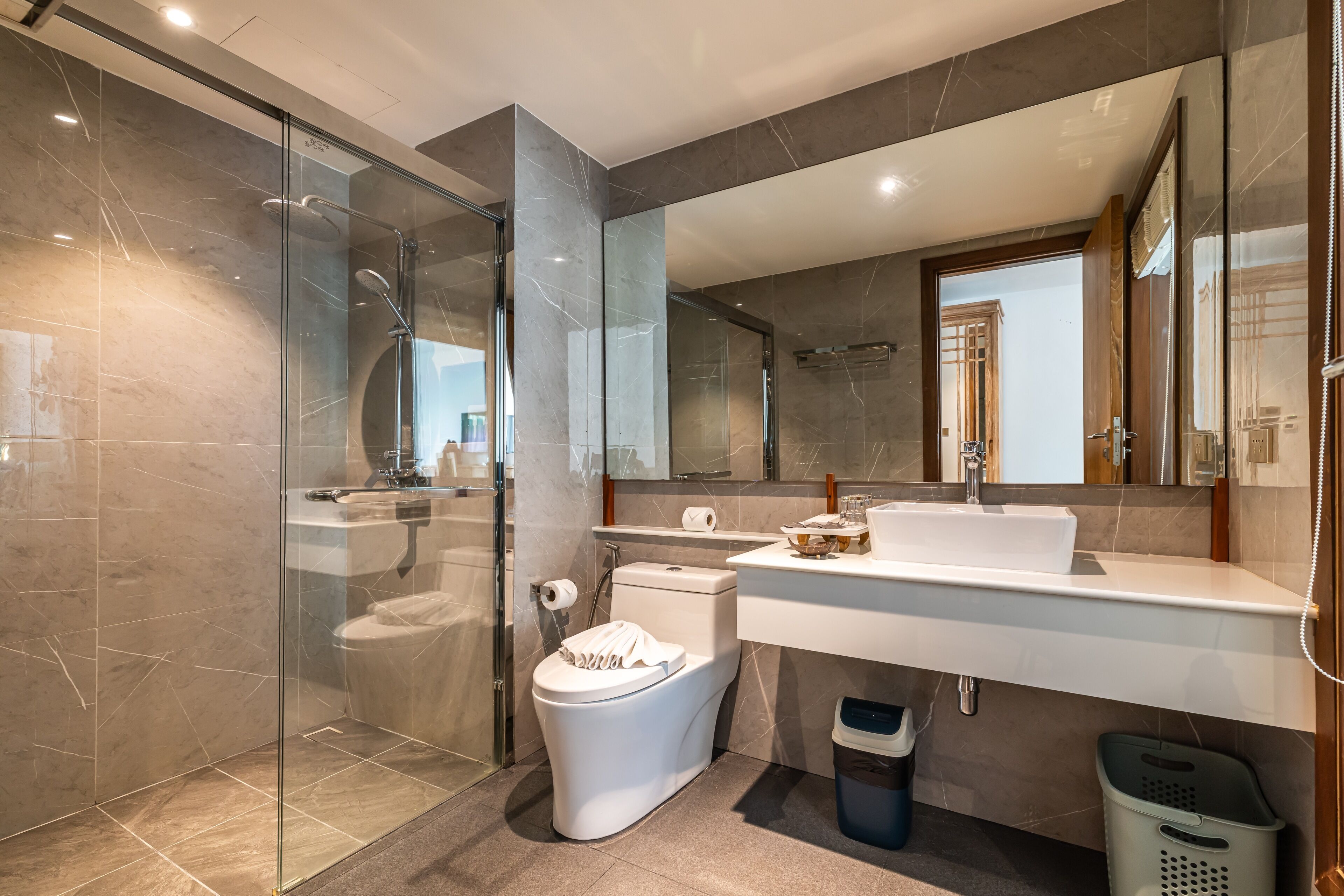 A modern bathroom with a glass-enclosed shower, a white toilet, a large mirror, and a white sink.