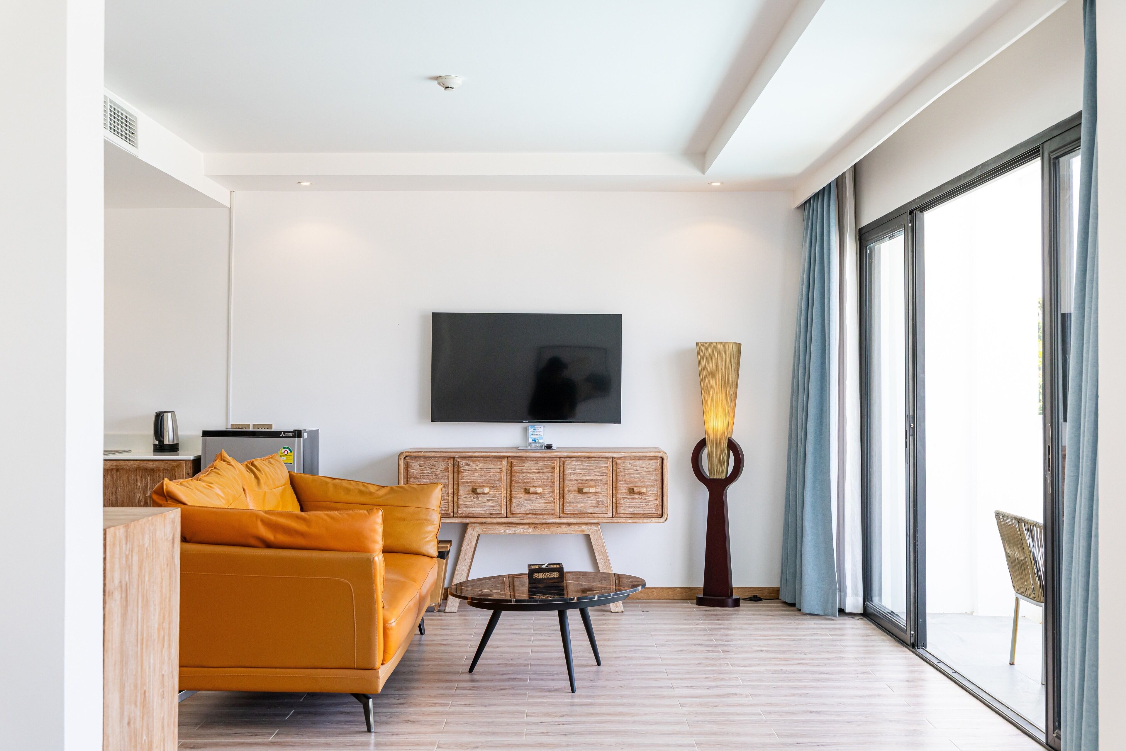 A modern living room with a sofa, a coffee table, a TV mounted on the wall, and a large window with curtains.