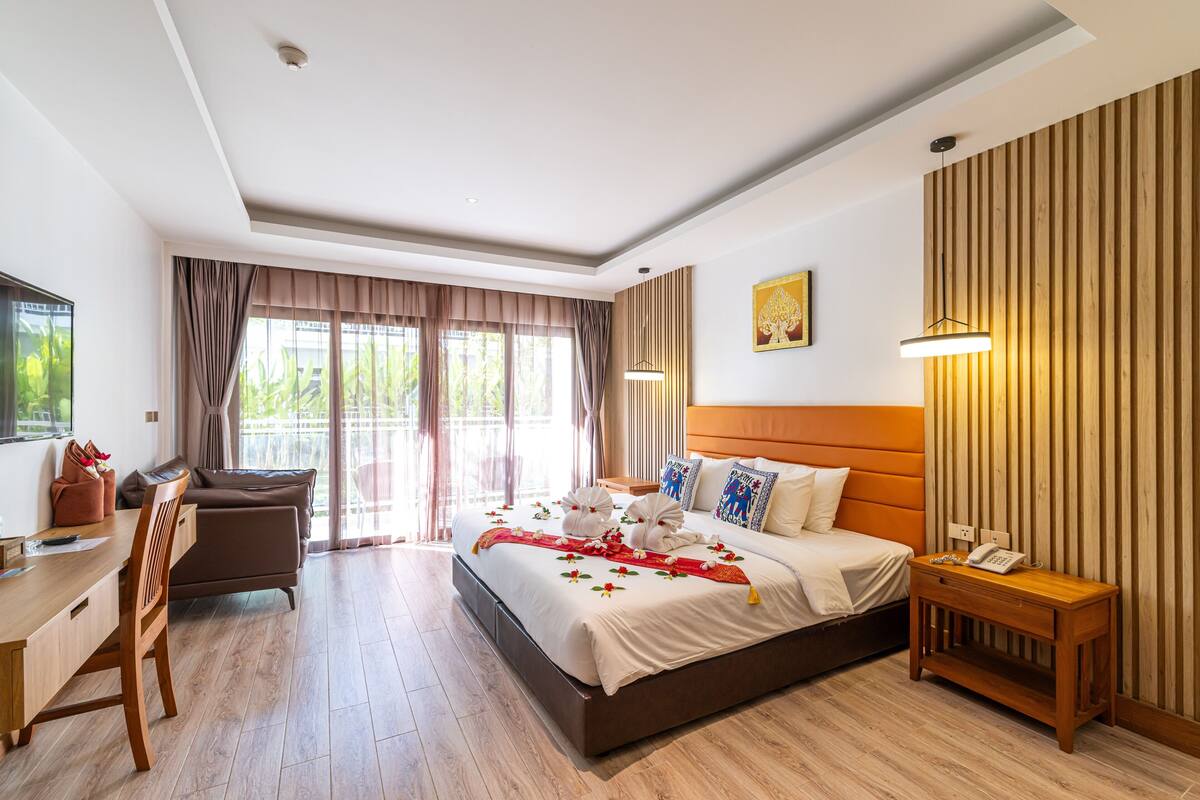 Ein Hotelzimmer mit Bett, Nachttisch, Schreibtisch, Stuhl und Blick ins Grüne durch das Fenster.