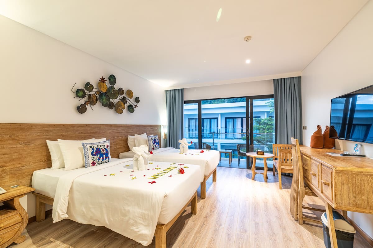 Ein Hotelzimmer mit zwei Betten, einem Holztisch, einem Fernseher und einem Balkon mit Stadtblick.