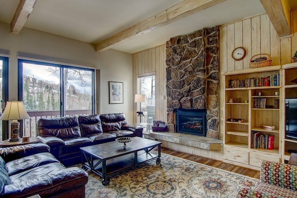 A cozy living room with a stone fireplace, leather sofas, a coffee table, and a bookshelf.