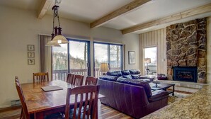 A spacious living area with a wooden dining table, leather sofa, and a stone fireplace. - Best Location - True Hike In/Out TH w/Private HotTub and Slope Views-Gas Fireplace-W/D in Unit (Steamboat Springs)