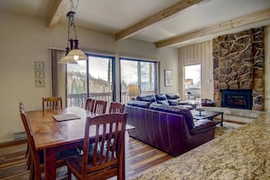 A spacious living area with a wooden dining table, leather sofa, and a stone fireplace.