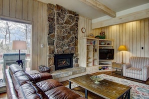 A cozy living room with a stone fireplace, leather sofa, wooden shelves, and a television.