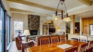 A spacious living area with a fireplace, wooden beams, a stone wall, and a dining table with chairs. - Best Location - True Hike In/Out TH w/Private HotTub and Slope Views-Gas Fireplace-W/D in Unit (Steamboat Springs)