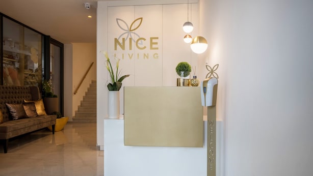Una recepción con un letrero que dice 'NICE LIVING', una escalera, un sofá y una planta en maceta.