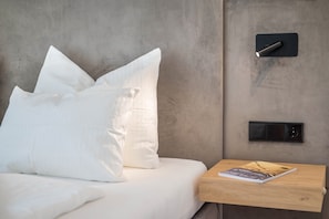 A bed with white bedding, a wooden bedside table with a magazine, and a wall-mounted control panel. - Modern Apartment "Nice 2" with Balcony in the Center of Bressanone/Brixen (Brixen)