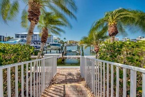 A pathway leading to a marina with boats, palm trees, and a clear sky.