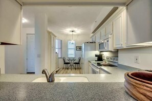 A kitchen with a granite countertop, a sink, a dining area with two chairs, and a window with blinds.