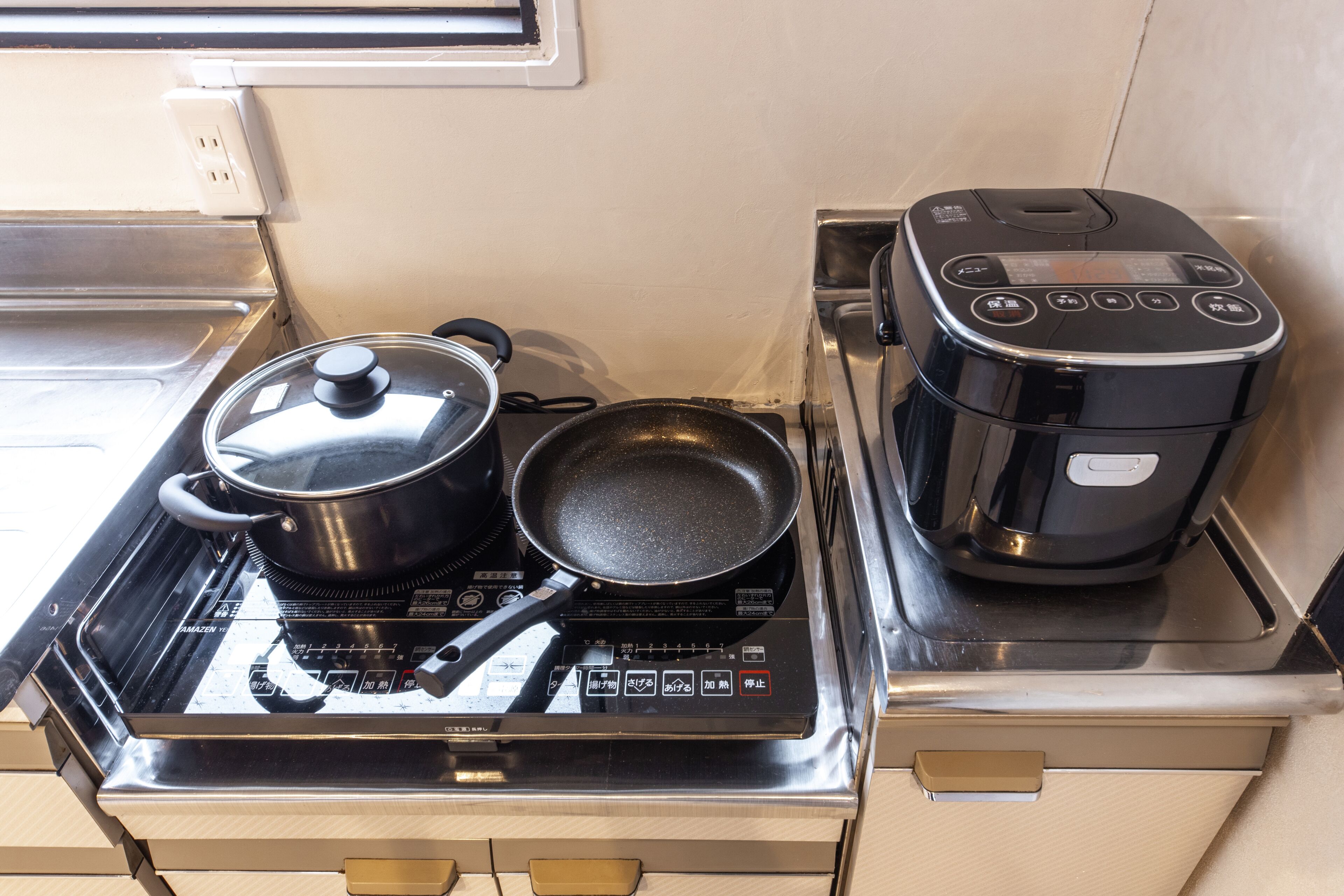 Une cuisine équipée d’une cuisinière, d’une casserole, d’une poêle et d’un cuiseur à riz.