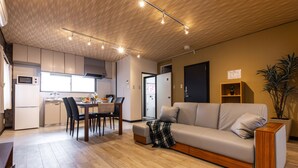 A modern kitchen with built-in appliances, a dining area with a table and chairs, and a living room with a sofa and a plant. - Urban Stay Oshiage (Tokyo)