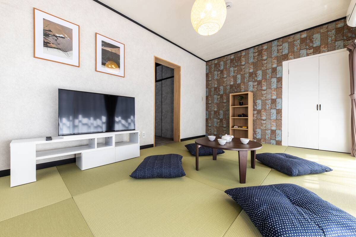 A modern living room with tatami flooring, a flat-screen TV, a wooden table with teaware, and a wardrobe.