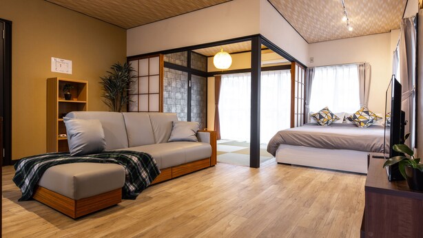 A modern, compact living space with a sofa, a bed, a wooden floor, and a ceiling with recessed lighting. - Urban Stay Oshiage (Tokyo)