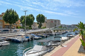 A marina with various boats docked, a pedestrian bridge, and buildings in the background. - Eclari - Javea, Costa Blanca (Javea)