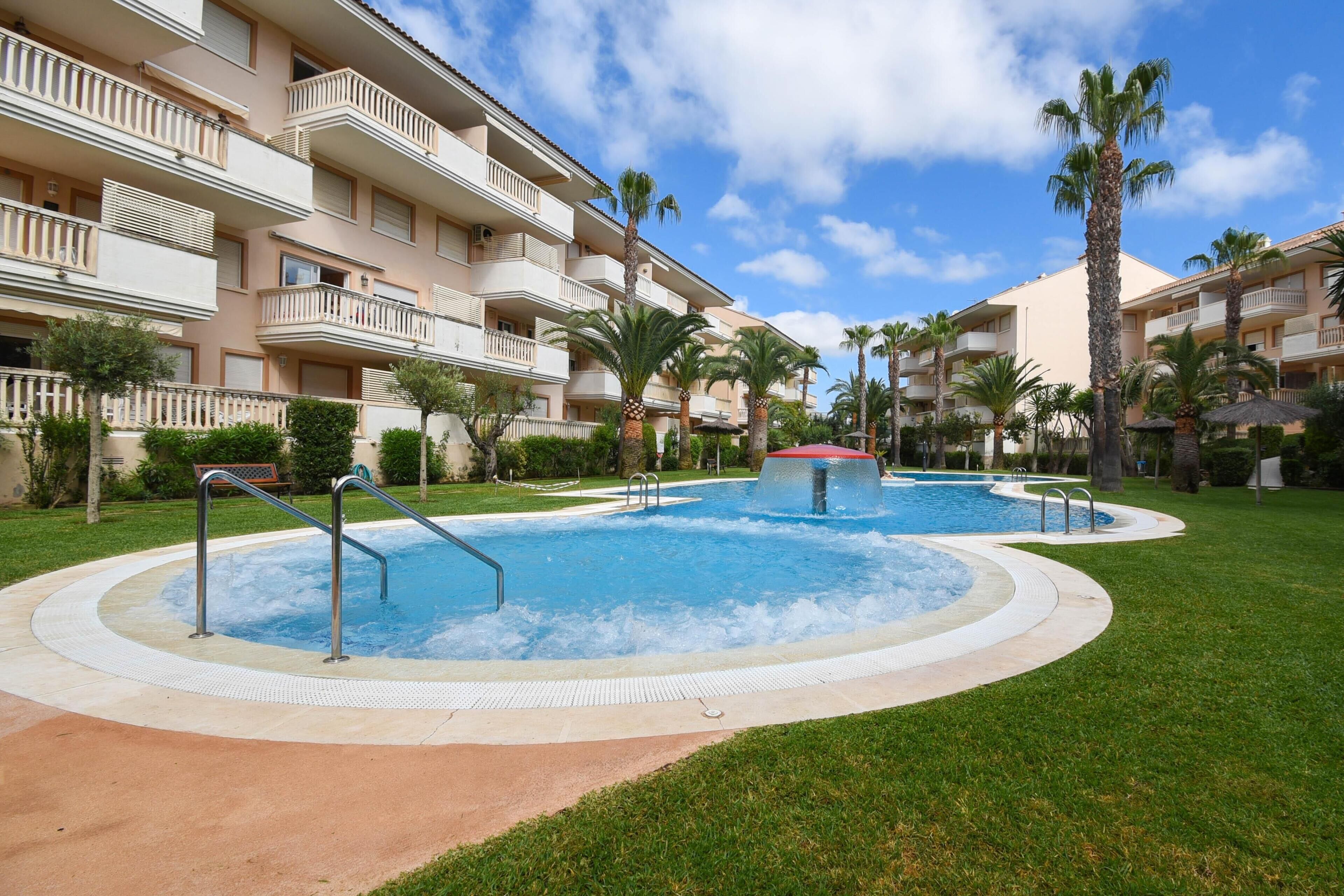 A hotel with a pool area, palm trees, and a clear blue sky.