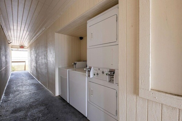 A laundry room with two stacked washers and dryers, wooden walls, and a concrete floor. - Red Roof Inn Houston North - Fm1960 and I-45 (Houston)
