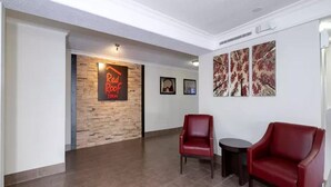 A lobby with a red brick wall, two red leather chairs, a small round table, and framed artwork on the wall. - Red Roof Inn Houston North - Fm1960 and I-45 (Houston)