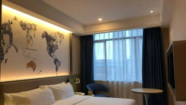 A hotel room with a large bed, a desk, a chair, a small table, and a world map on the wall.