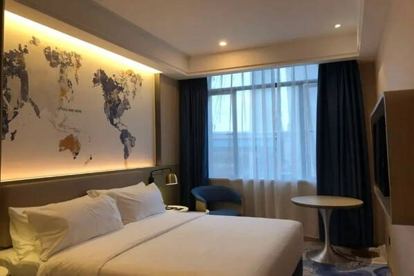 A hotel room with a large bed, a desk, a chair, a small table, and a world map on the wall.