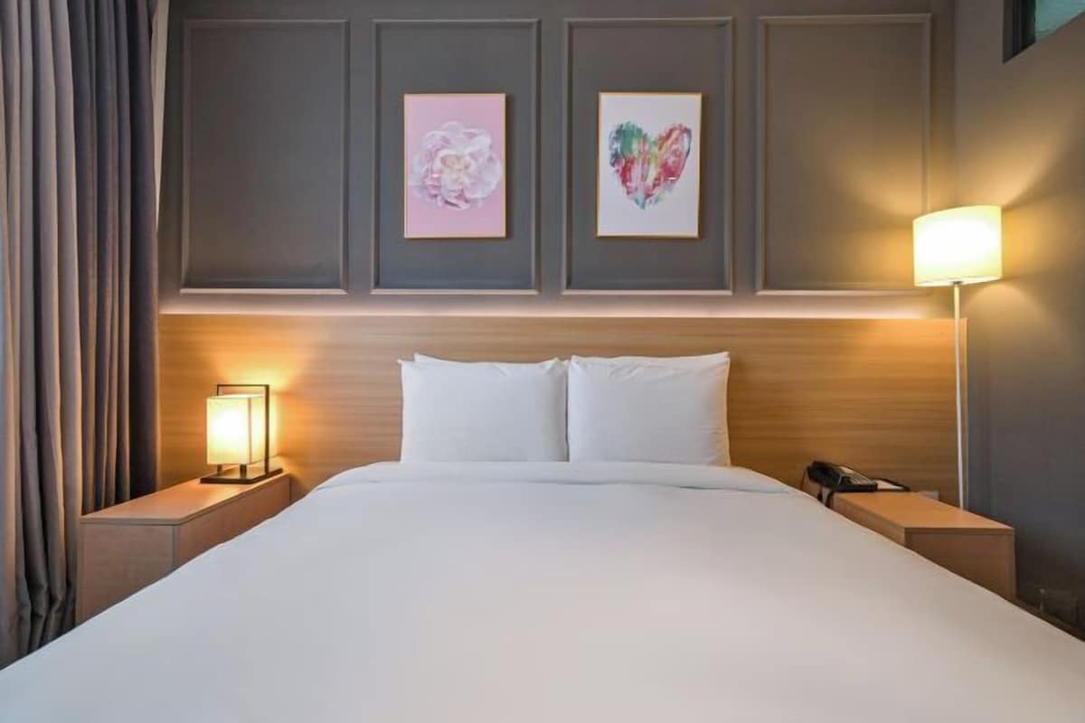 Ett hotellrum med en stor säng, två sängbord, en lampa och två inramade konstverk på väggen.
