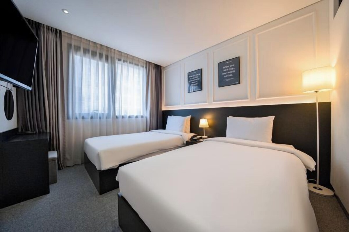 Ett hotellrum med två sängar, en TV, ett skrivbord och en lampa.