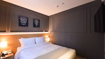 Une chambre d’hôtel avec un lit soigneusement fait, deux lampes de chevet, un téléphone sur la table de chevet et des affiches motivantes accrochées au mur.