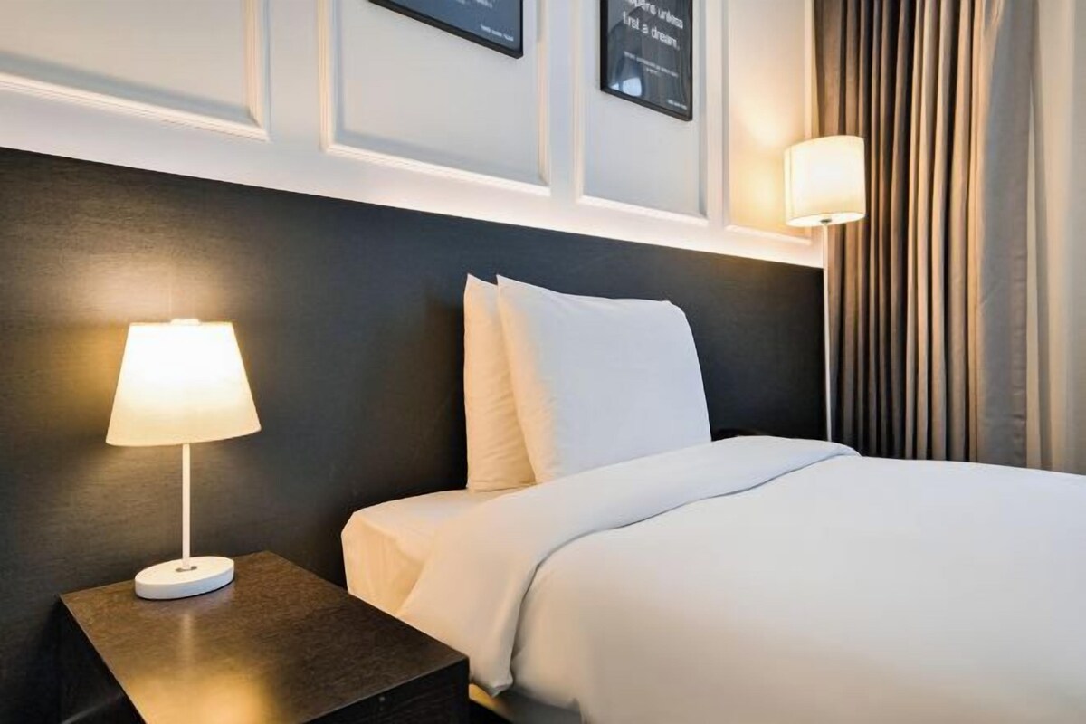 A hotel room with a neatly made bed, a bedside lamp, and a framed quote on the wall.