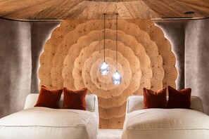 Une pièce dotée d’un décor mural en bois original, de deux canapés blancs avec des coussins marron et de luminaires suspendus.