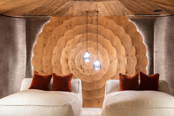 Une pièce dotée d’un décor mural en bois original, de deux canapés blancs avec des coussins marron et de luminaires suspendus.