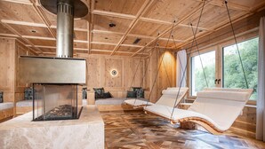 A wooden cabin interior with a fireplace, wooden flooring, and two lounge chairs by a large window. - Kuschel-chalet - Chalets Grossmitt (Pertisau)