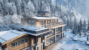 Un bâtiment moderne à plusieurs étages, doté d’une façade en verre, d’une terrasse en bois et offrant une vue sur une forêt enneigée.