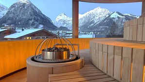 A modern outdoor seating area with a stone fire feature and a view of snow-capped mountains. - Kuschel-chalet - Chalets Grossmitt (Pertisau)