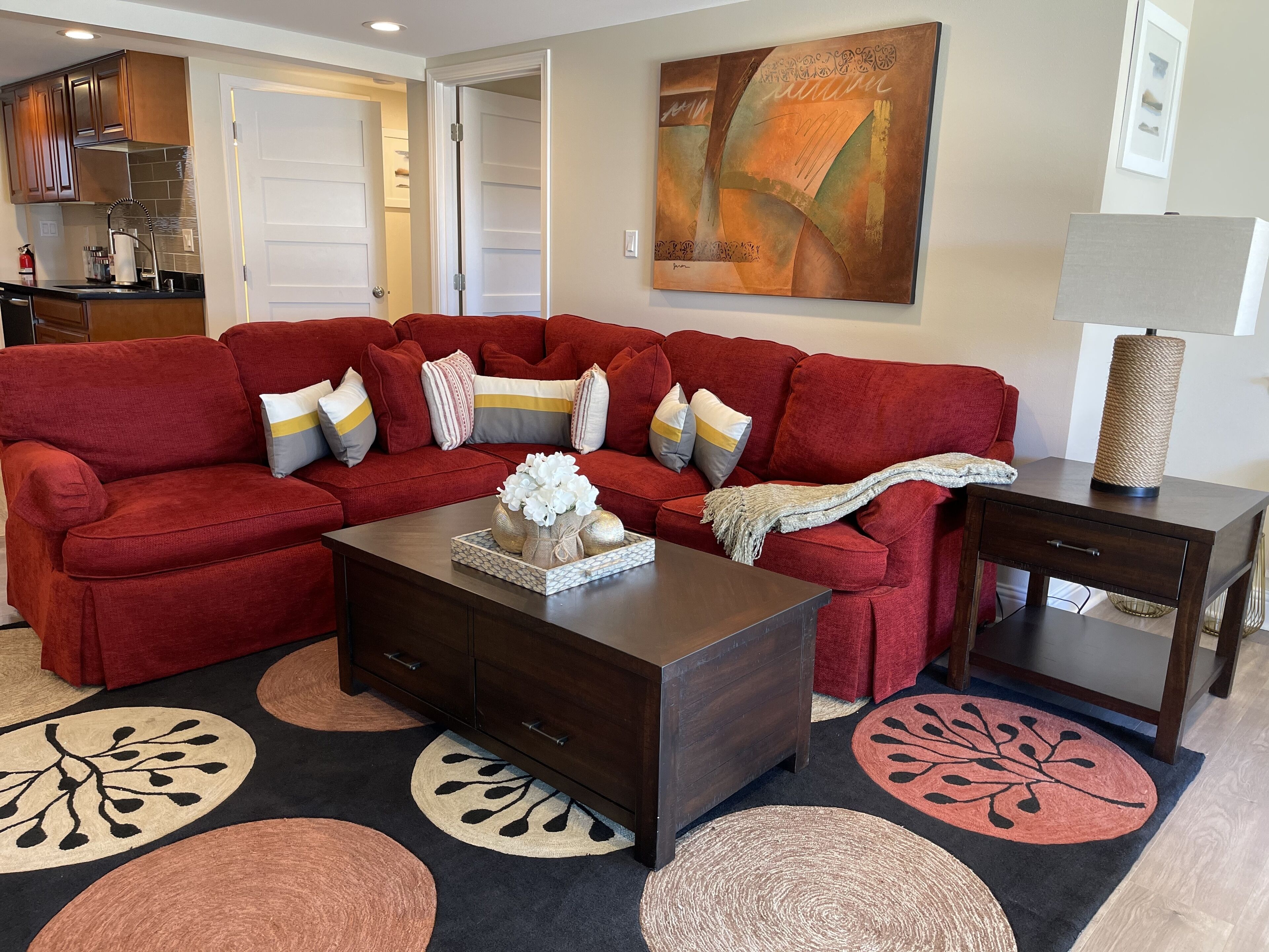 A living room with a red sectional sofa, a coffee table, and a side table. There is a painting on the wall and a lamp on the side table.