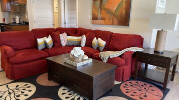 A living room with a red sectional sofa, a coffee table, and a side table. There is a painting on the wall and a lamp on the side table.