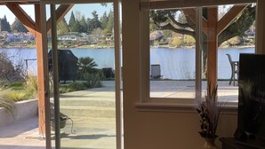Une pièce dotée de grandes fenêtres donnant sur un lac, avec un patio et une vue sur des maisons au loin.