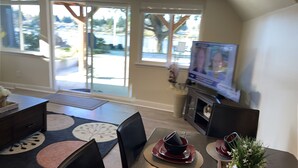 Un coin repas avec une table dressée pour quatre personnes, un téléviseur fixé au mur et de grandes fenêtres donnant sur l’extérieur.