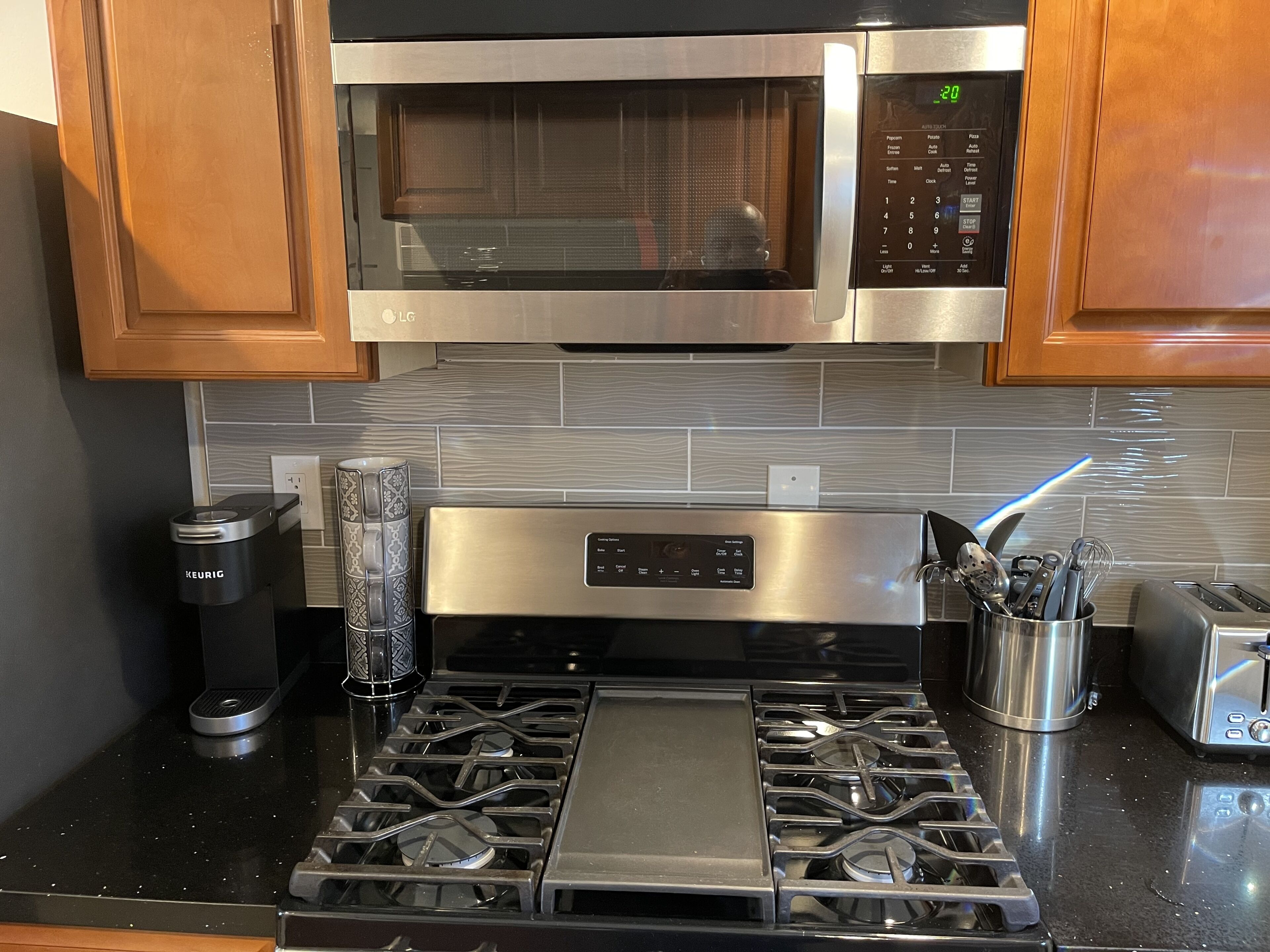 A kitchen with a stainless steel microwave, a Keurig coffee maker, a toaster, and a gas stove.