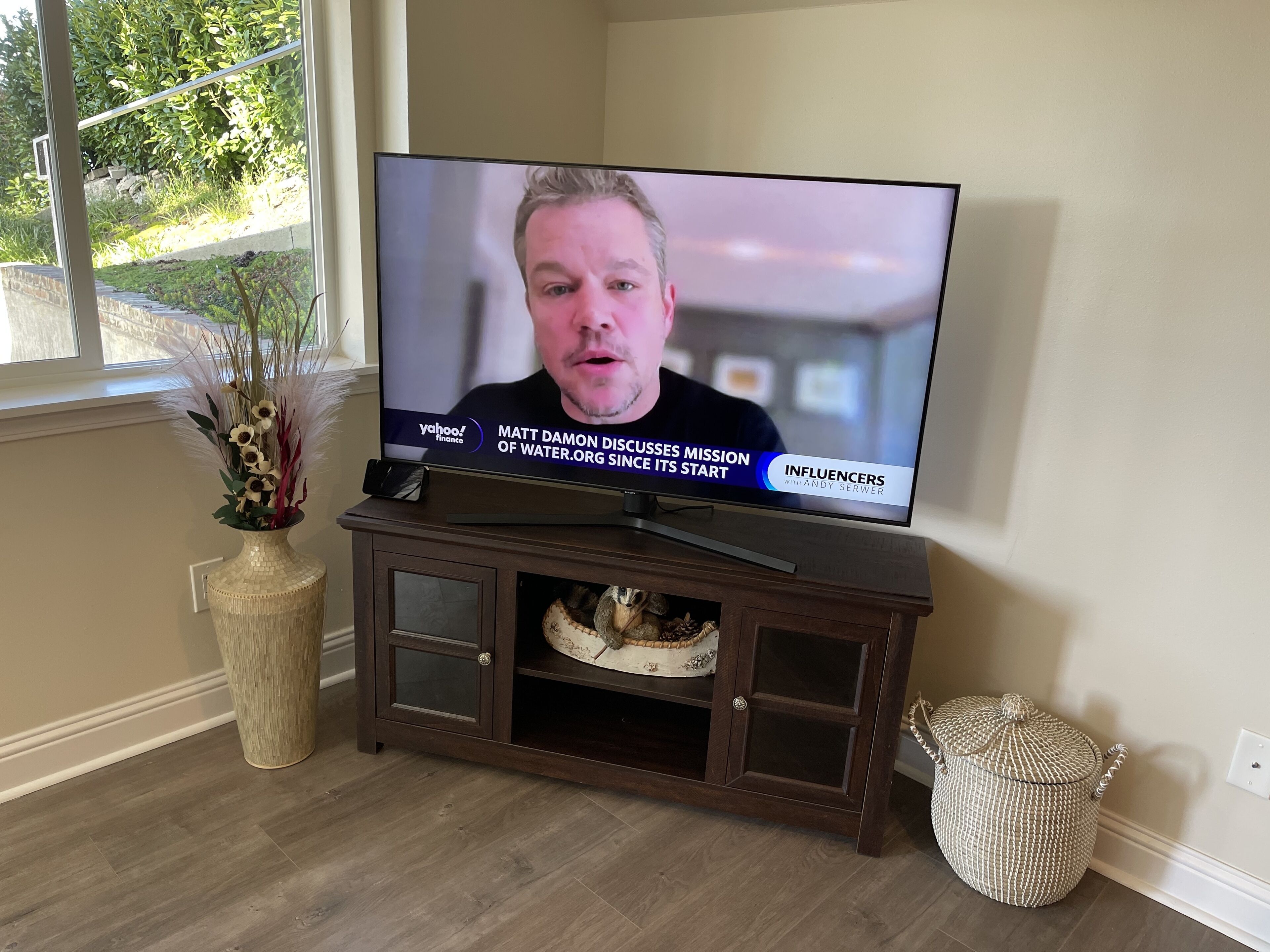A television on a wooden stand displaying a news program.