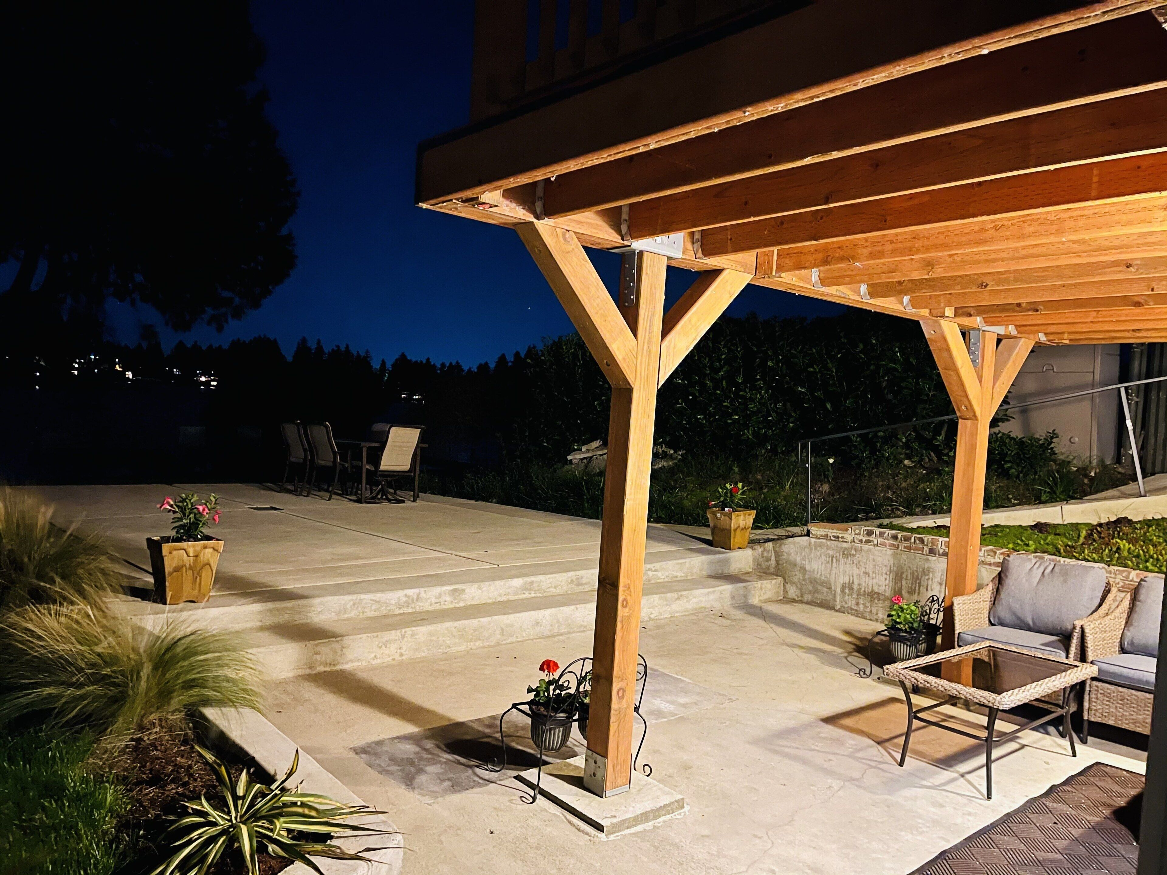 En uteplats med en träpergola, sittplats och krukväxter.