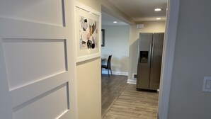 Un couloir doté d’un plancher en bois, de murs blancs et d’un réfrigérateur en acier inoxydable.